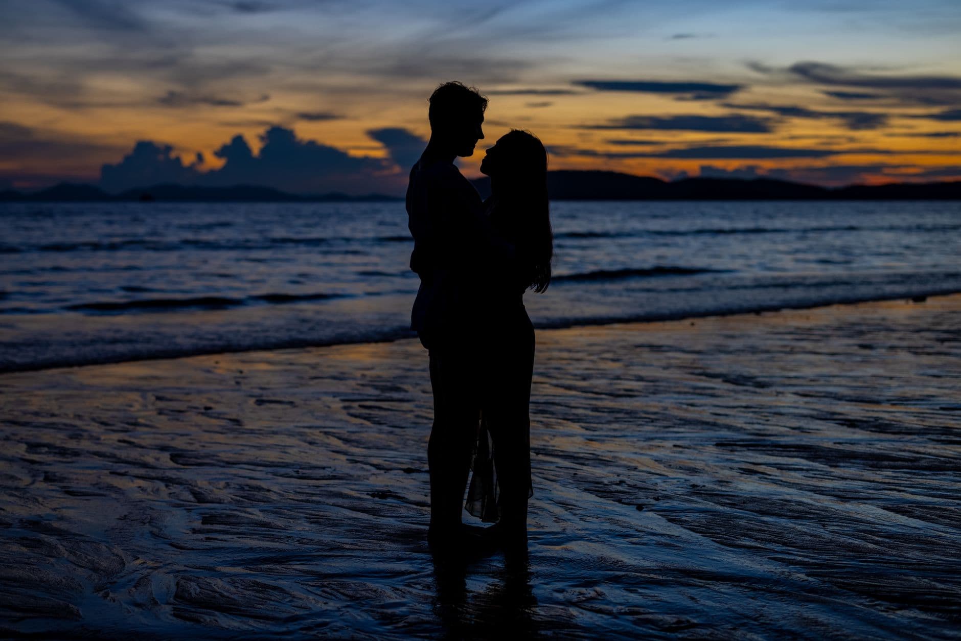 Pareja en silueta abrazada frente al mar al anochecer